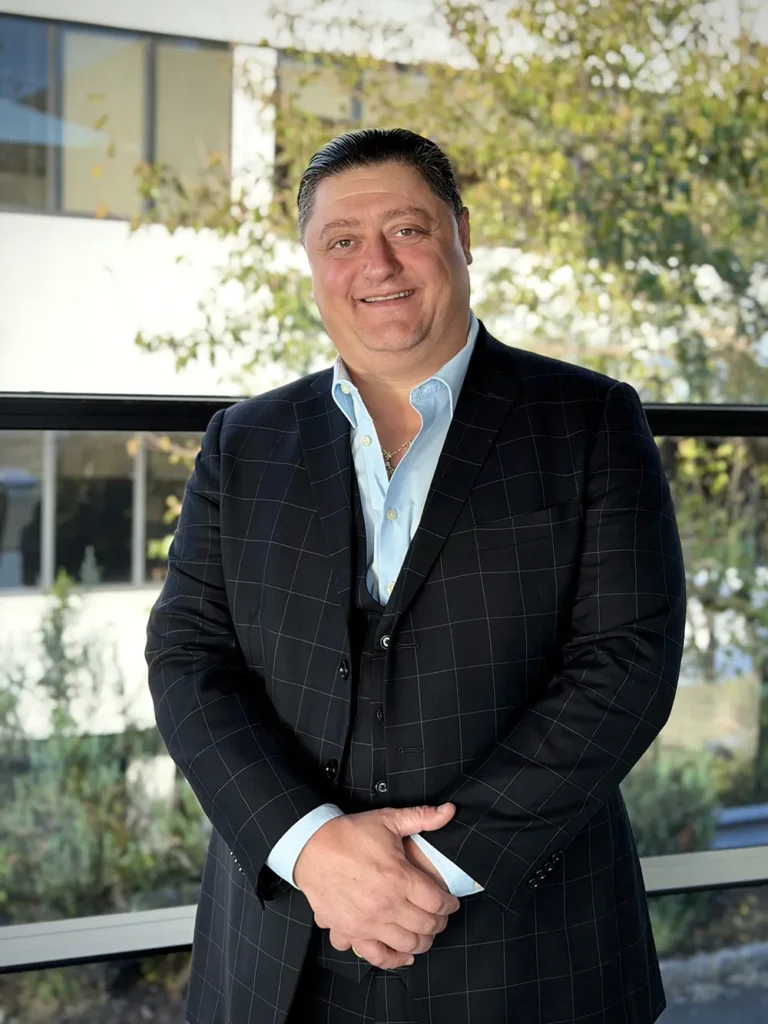 Smiling professional in a dark check suit standing by a window with hands folded